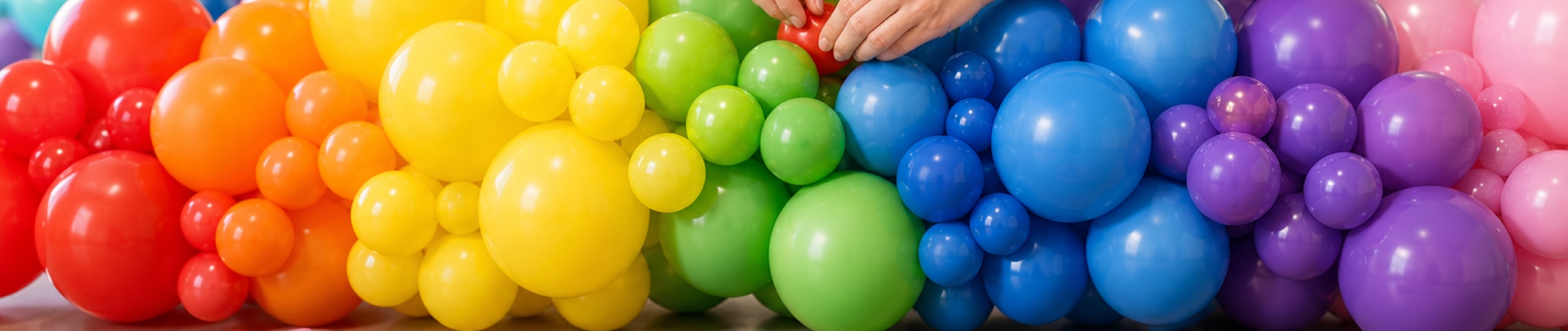 Hands assembling a rainbow organic balloon garland on a workbench